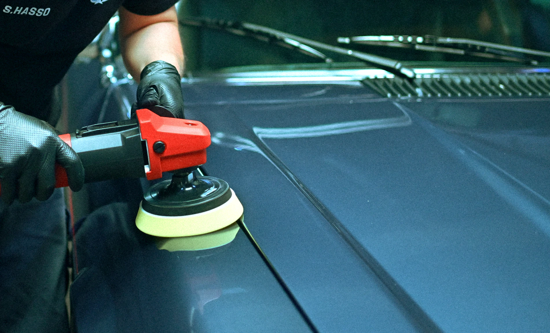 A detailer polishing the hood of a blue car